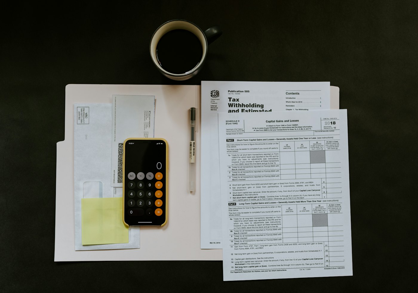 A phone calculator, a coffee cup and tax paperwork on a desk