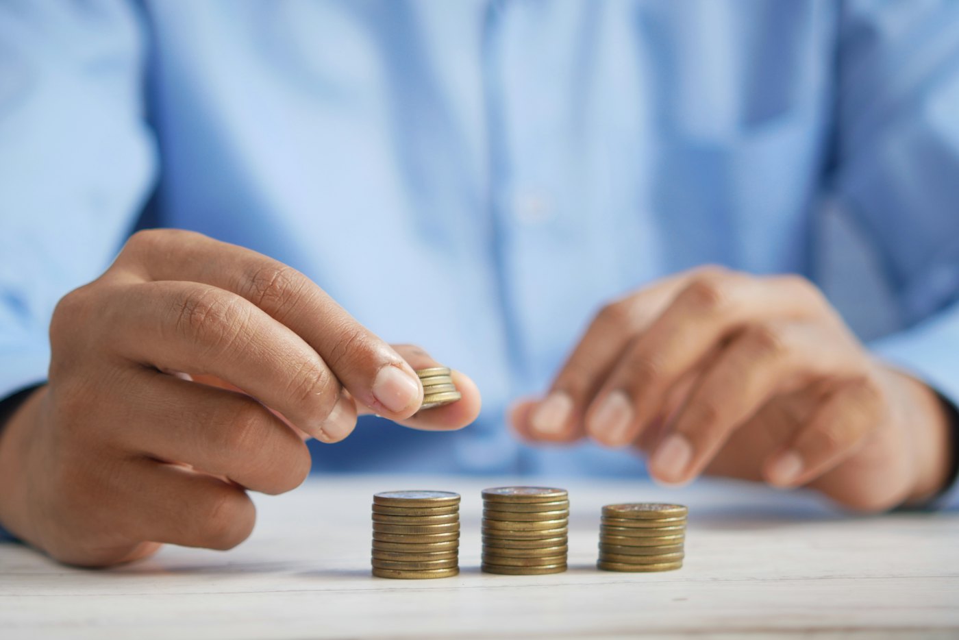 A person adding a coin to three growing stacks of coins on a table