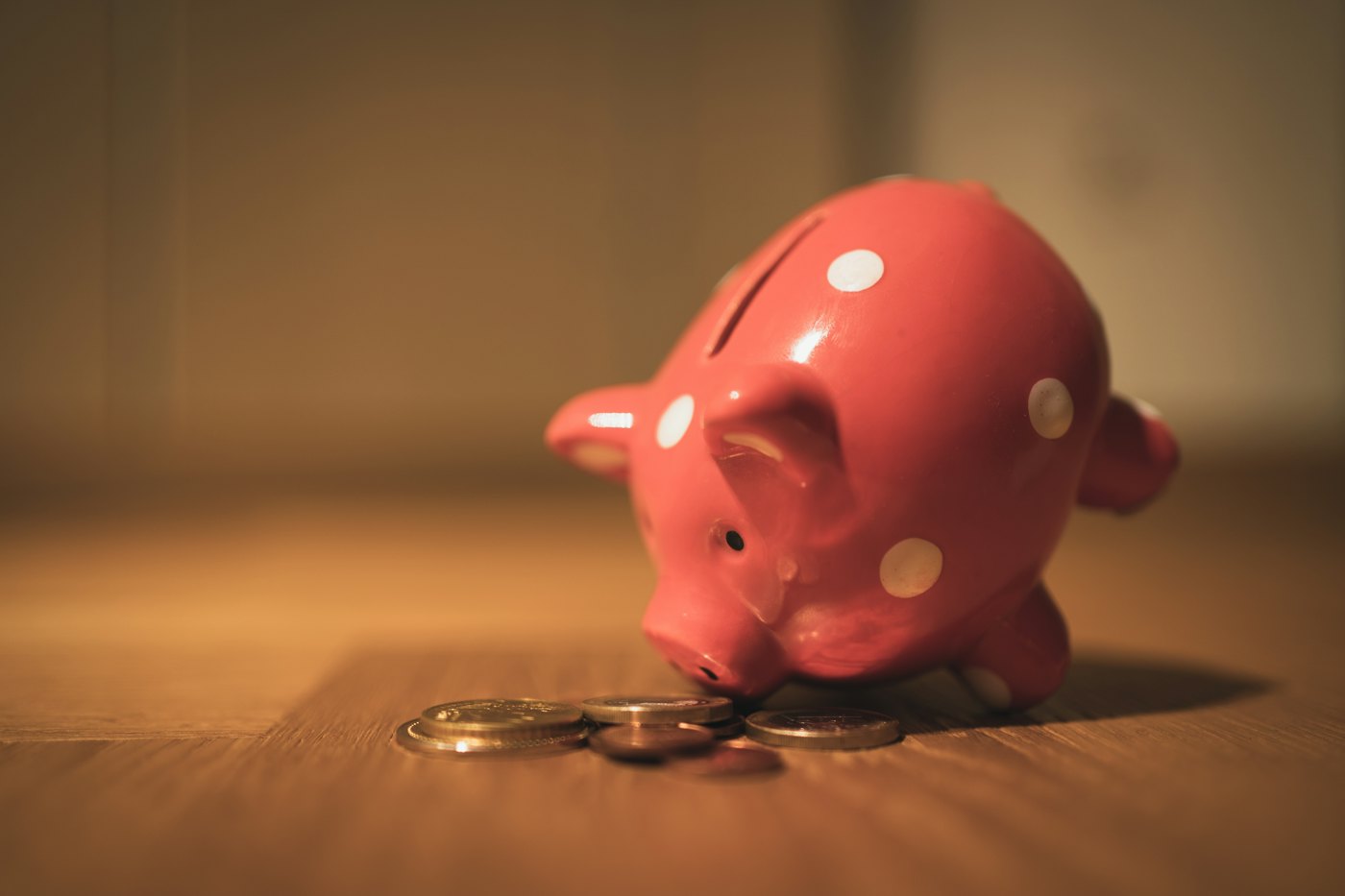 A pink piggy bank tipped forward beside a small pile of coins