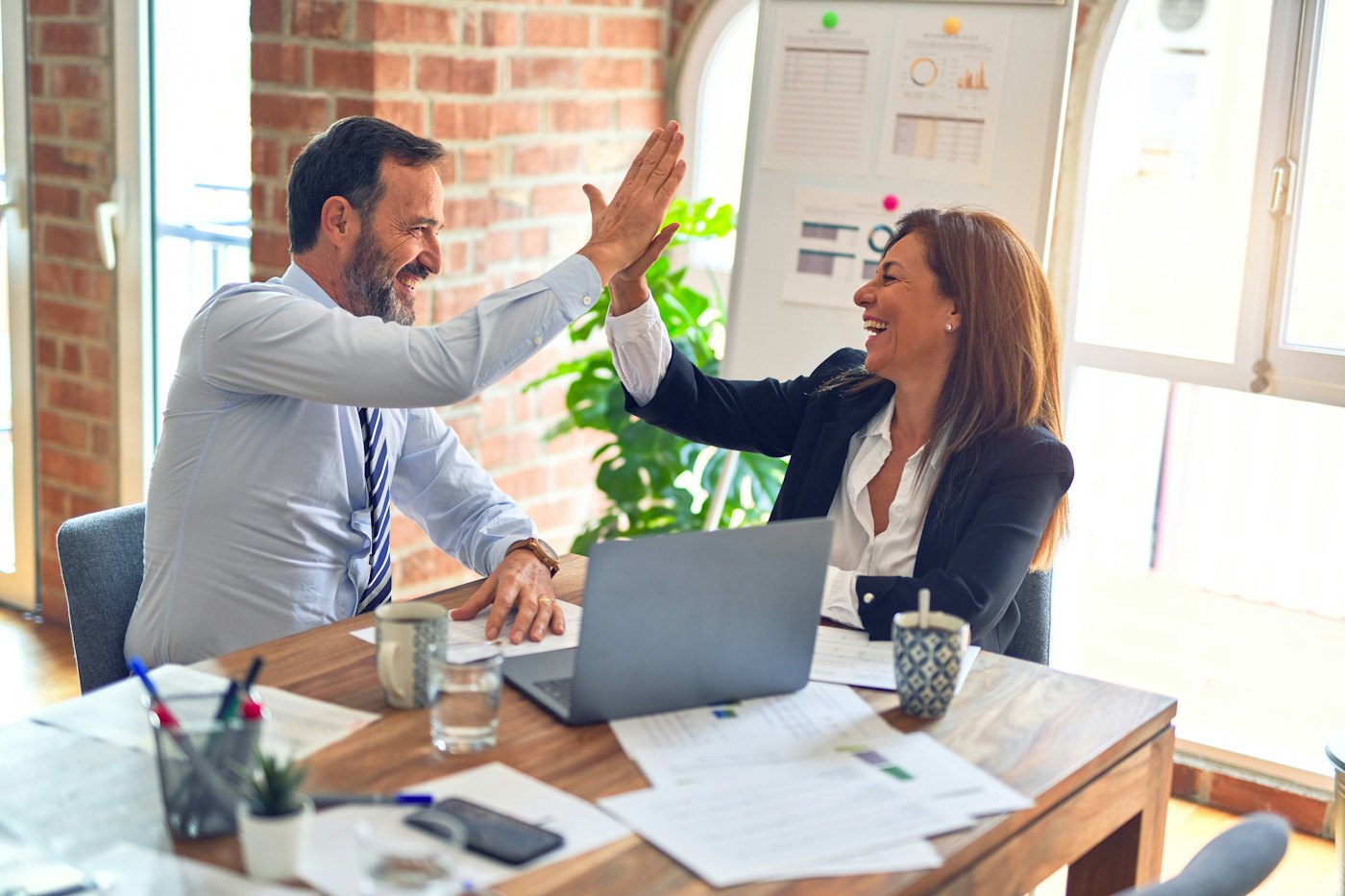 Two colleagues celebrating at a desk covered in printed reports